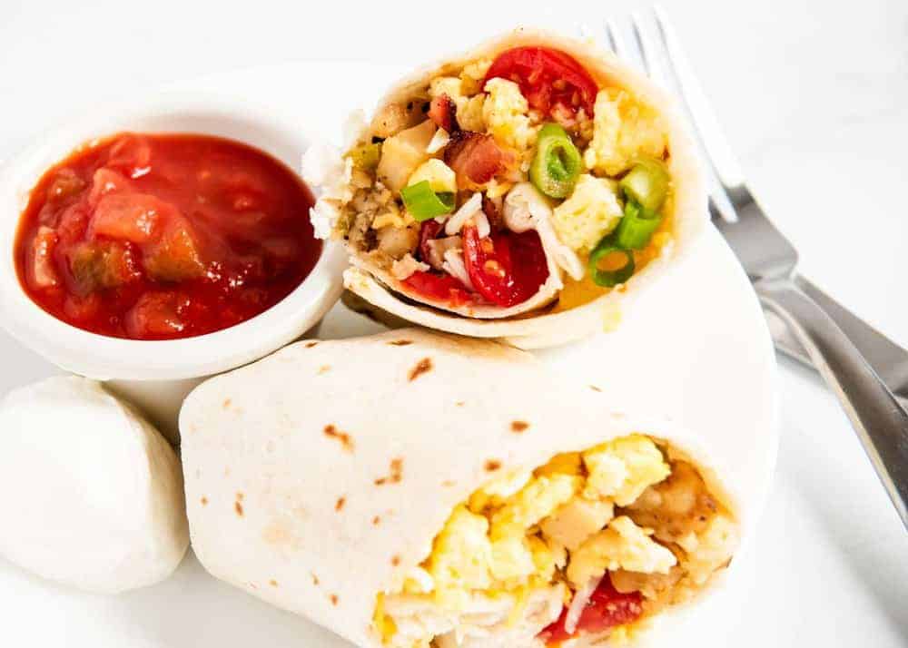 Breakfast burritos sliced in half on a white plate.