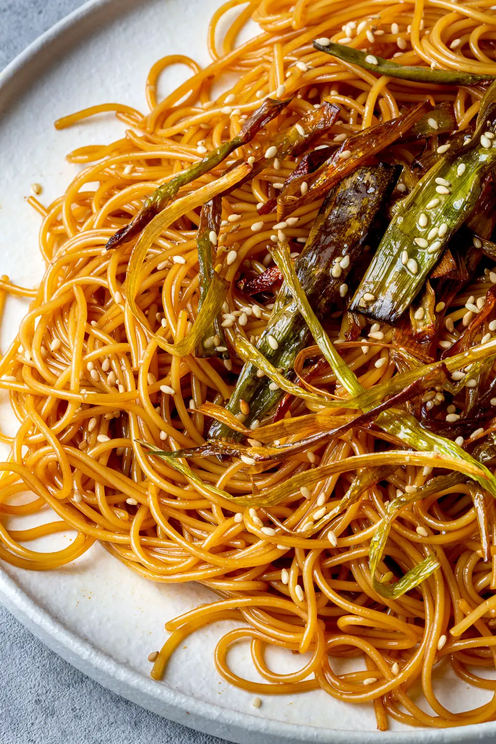 Fried spring onion with noodles on a light colored plate.