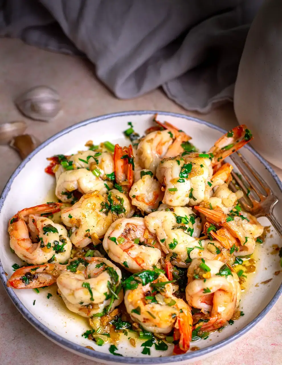 Garlic butter prawns on a white plate with a fork.