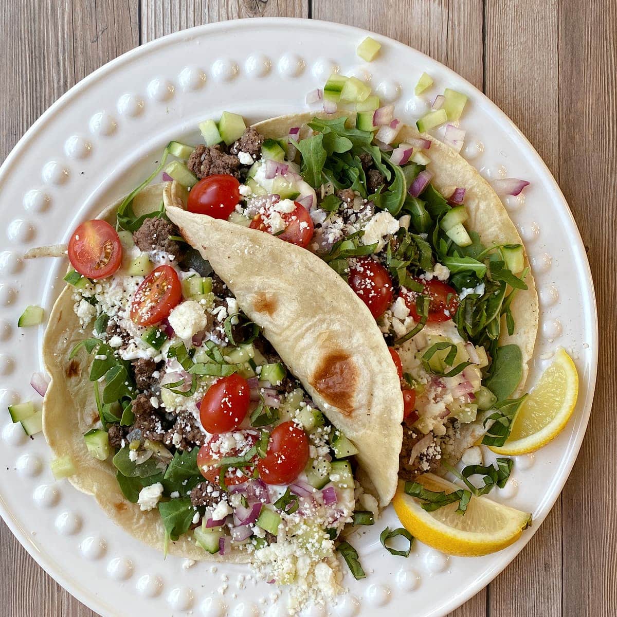 Greek tacos with lettuce, tomatoes, and onions on a white plate.