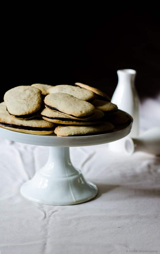 Homemade Milano cookies on a white cake stand.