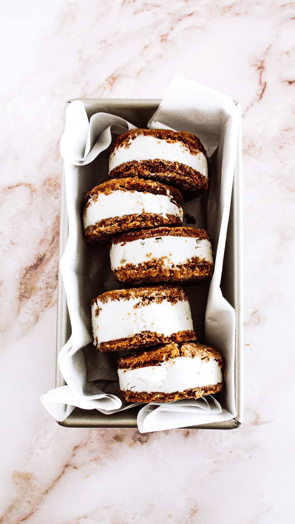 Ginger molasses cookie ice cream sandwiches in a parchment lined baking pan.