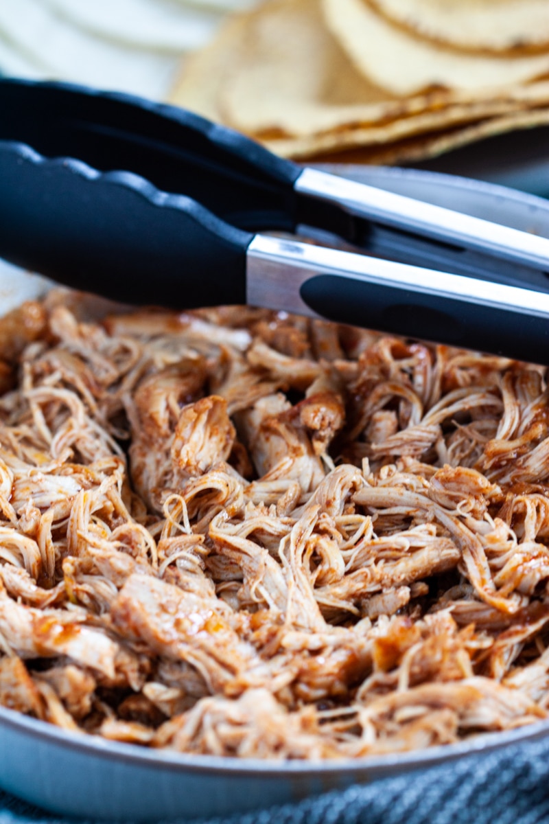 Tongs on top a dish filled with shredded instant pot salsa chicken.