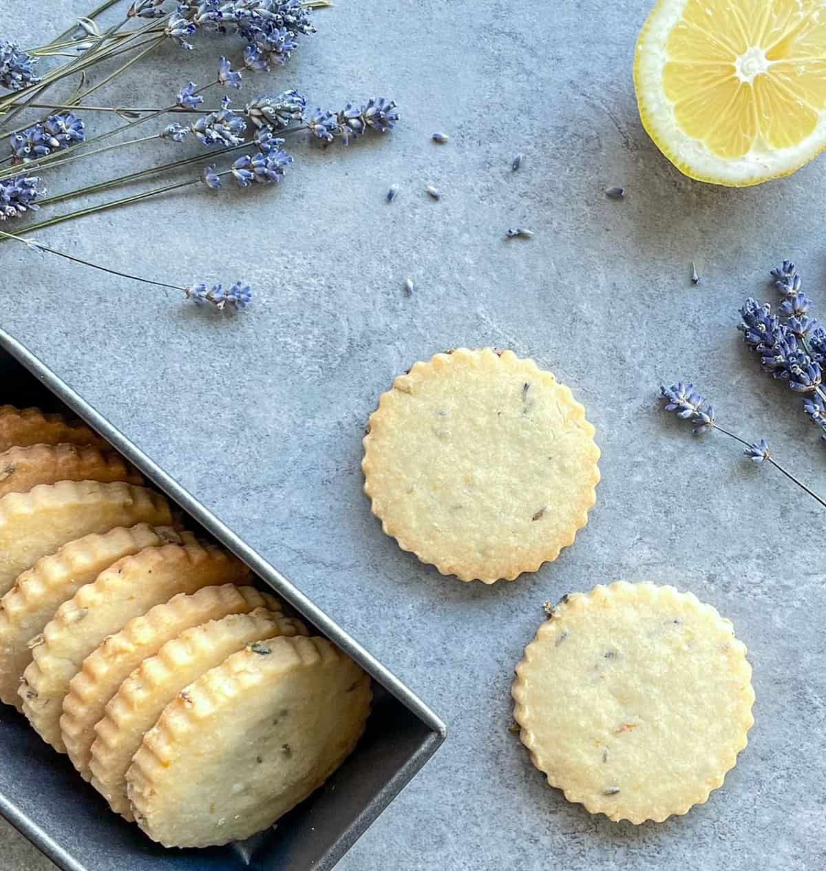 Lemon lavender shortbread cookies with sliced lemon and lavender in the background.