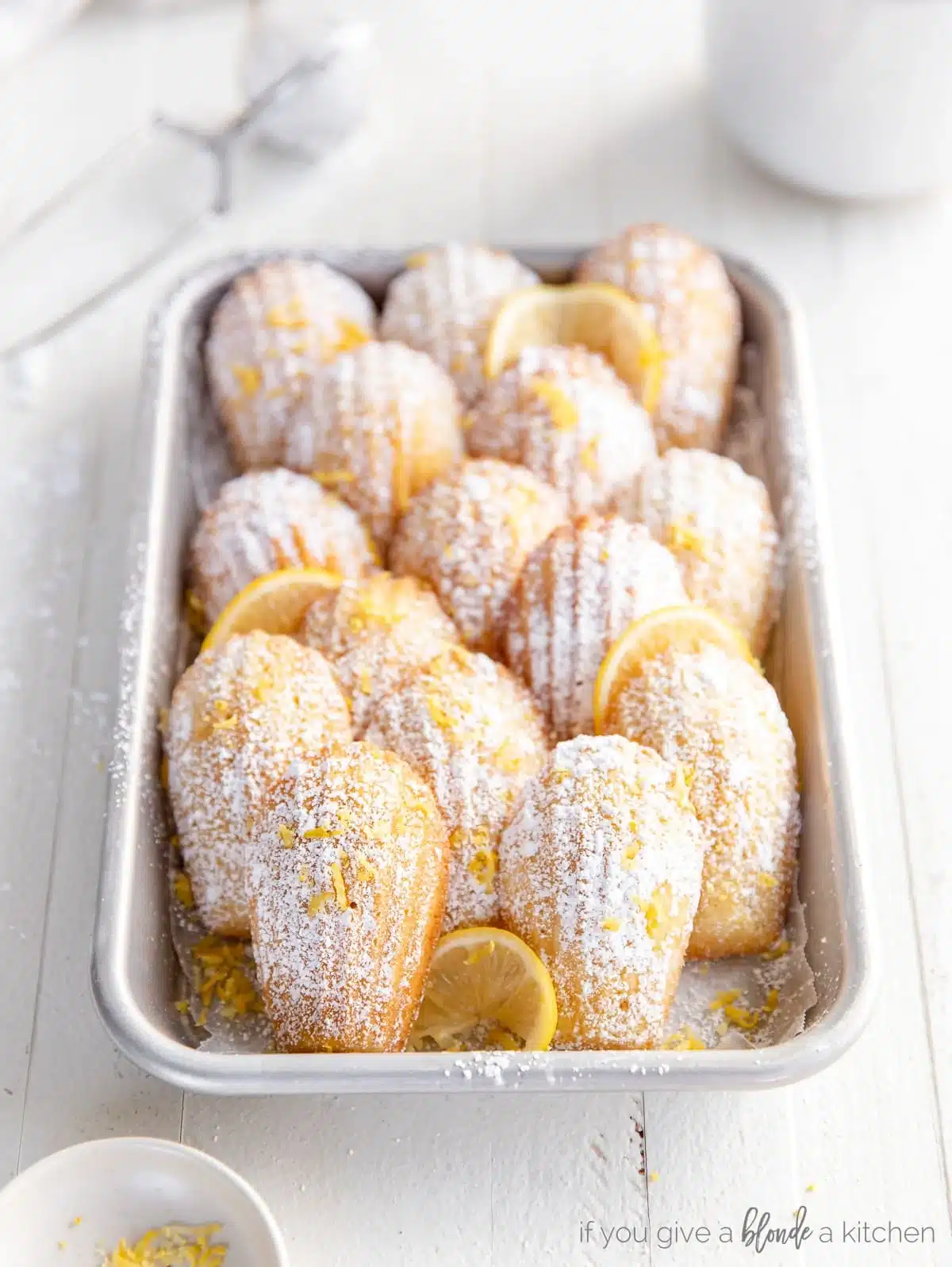 French Madeleine cookies dusted with powdered sugar and lemon zest in a silver tray.