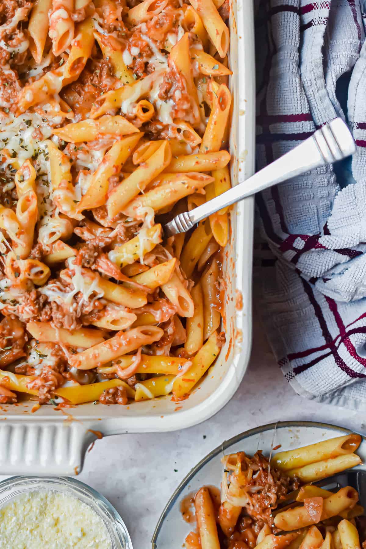 Meaty marinara pasta in a white baking dish with various effects in the background.