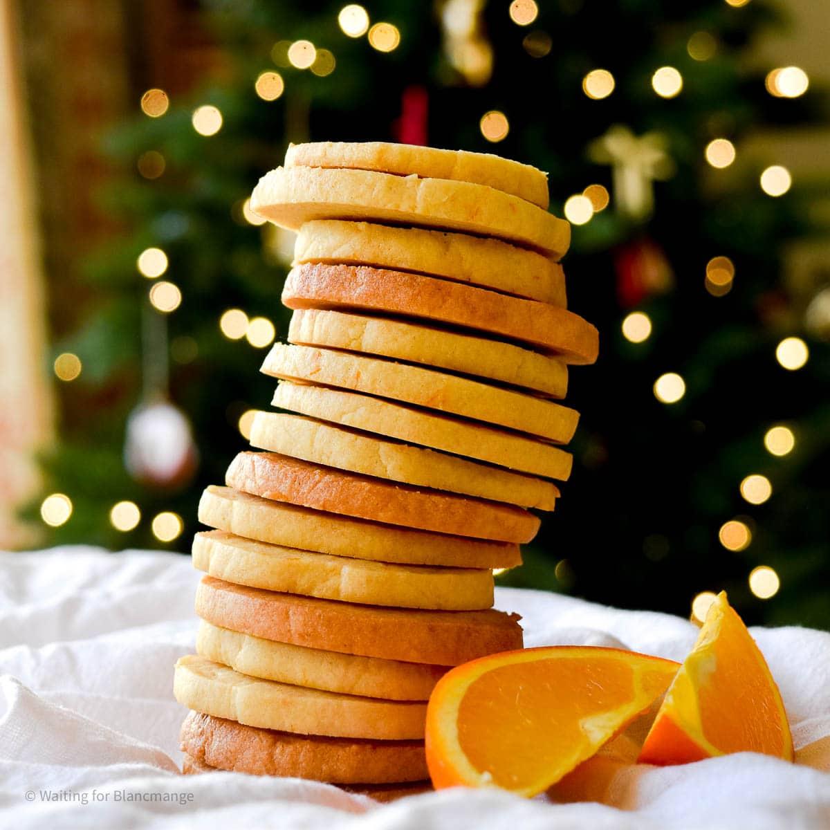 Stack of orange shortbread cookies with Christmas tree in the background.