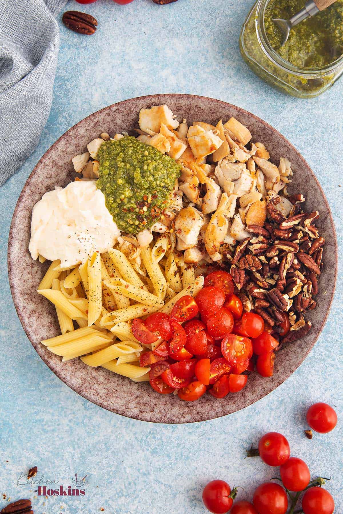 Cooked pasta, mayo, pasta, halved tomatoes, chopped pecans, and diced chicken in a light colored bowl.