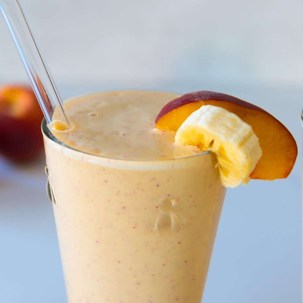 Closeup of peach smoothie in a glass with a straw.