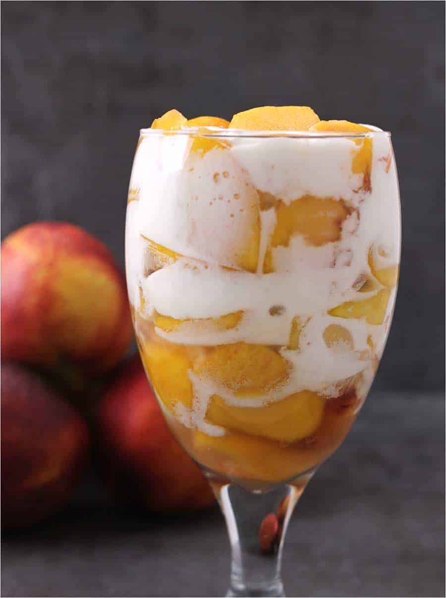 Peaches and cream in a glass with more peaches in the background.