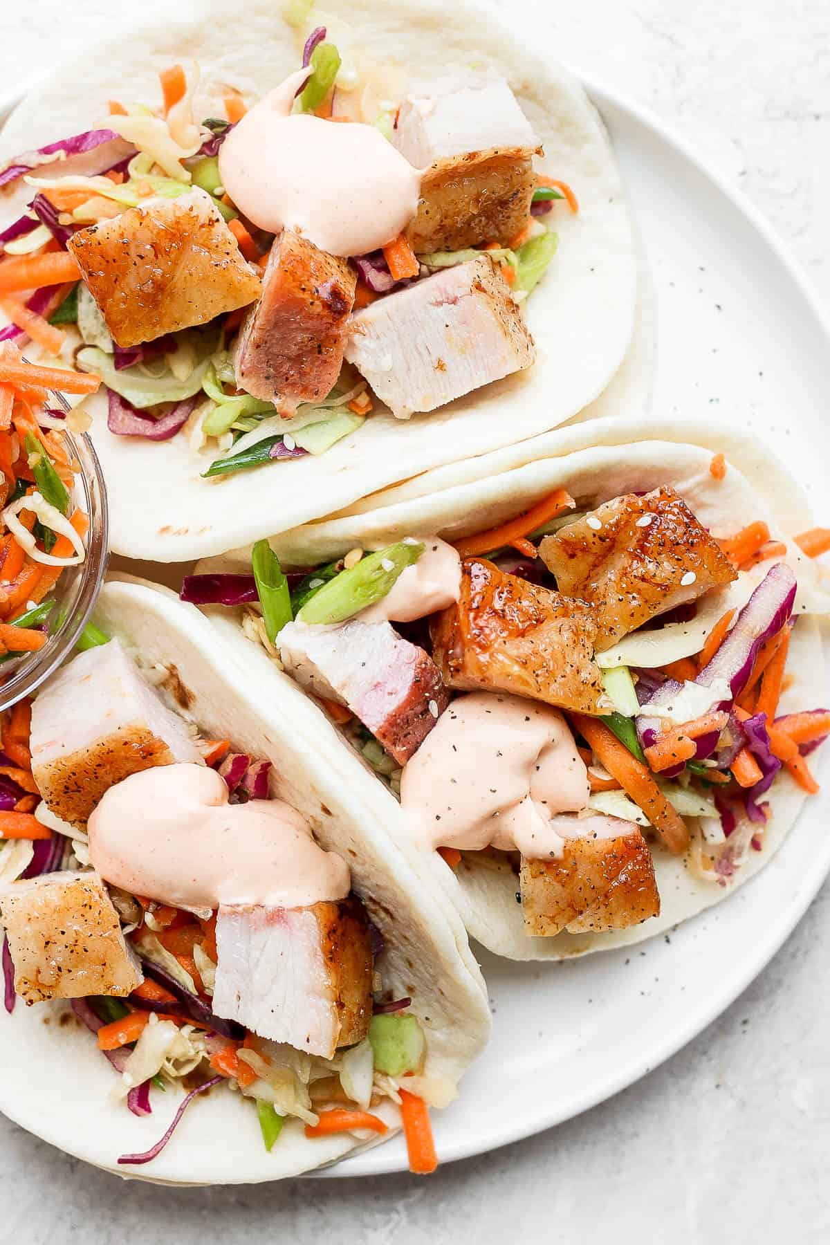 Pork belly tacos on a white plate.