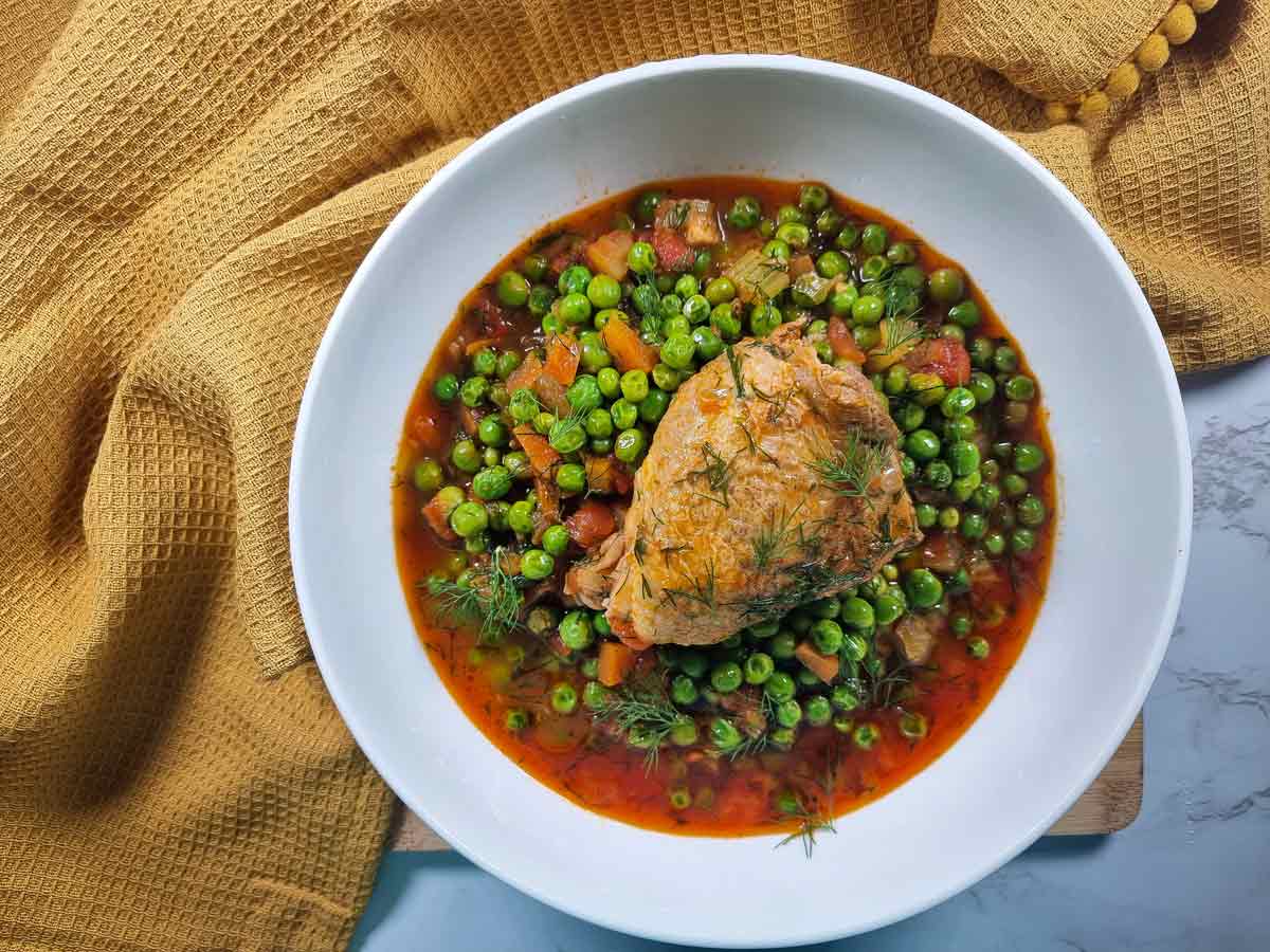 Romanian peas and chicken stew in a white bowl.