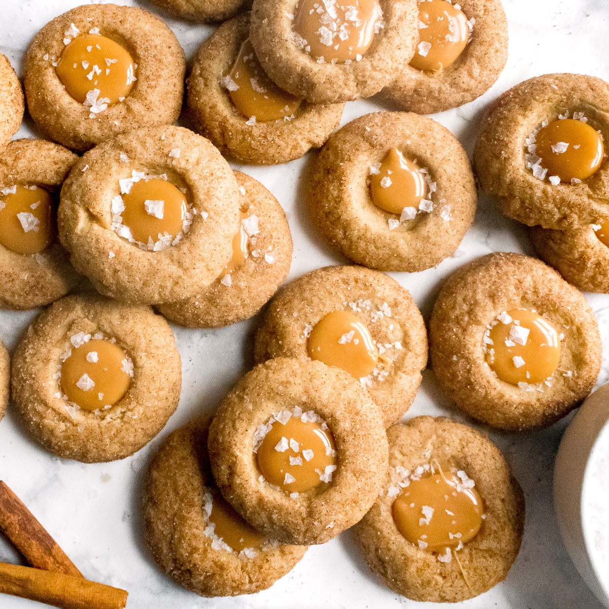 Salted caramel thumbprint cookies with cinnamon sticks in the background.