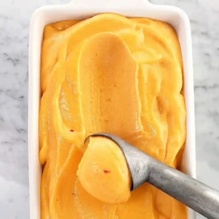 Peach sorbet in a baking dish with ice cream scoop.