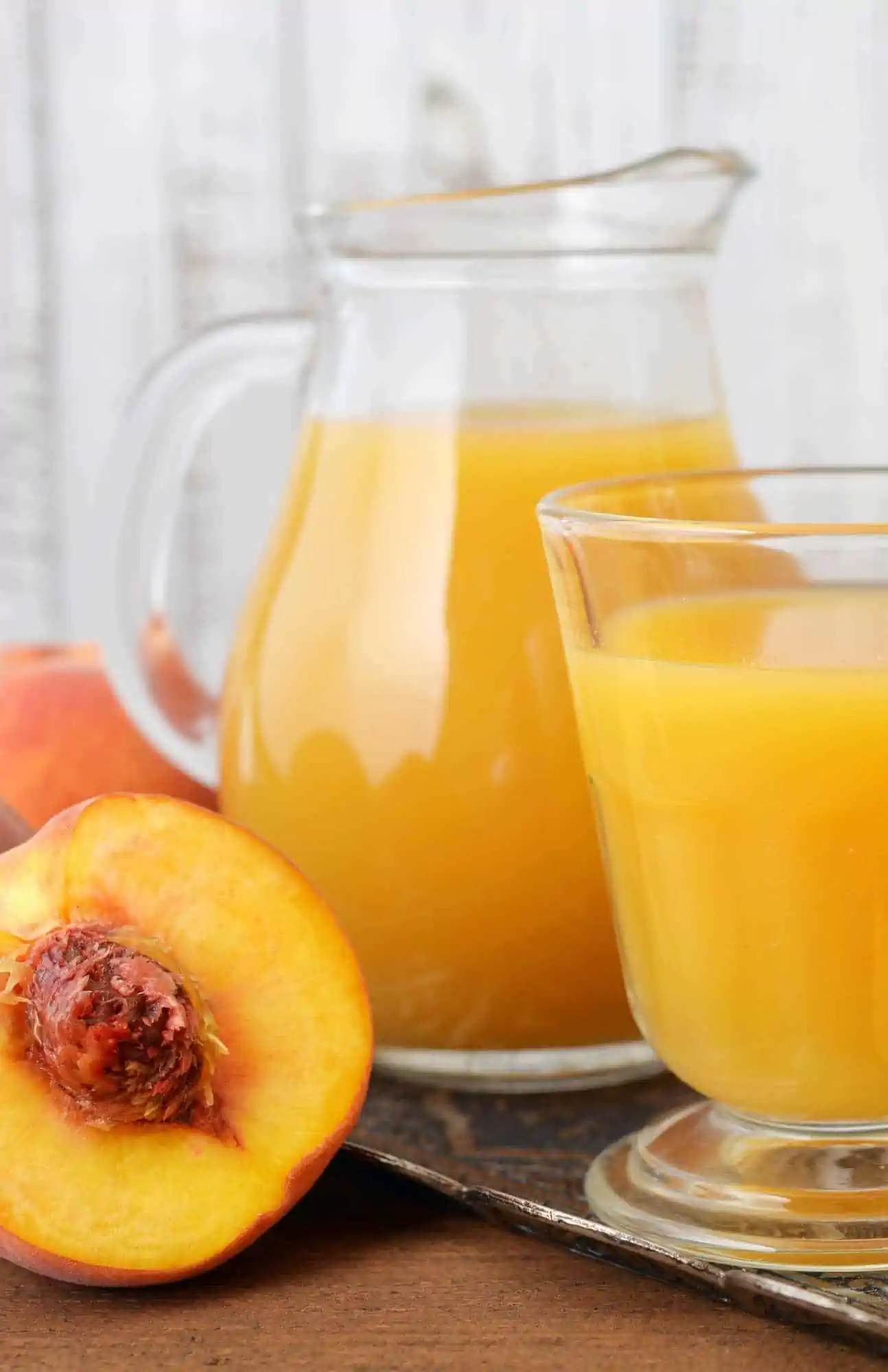 Fresh peach juice in a pitcher with peach and more juice served in a glass.