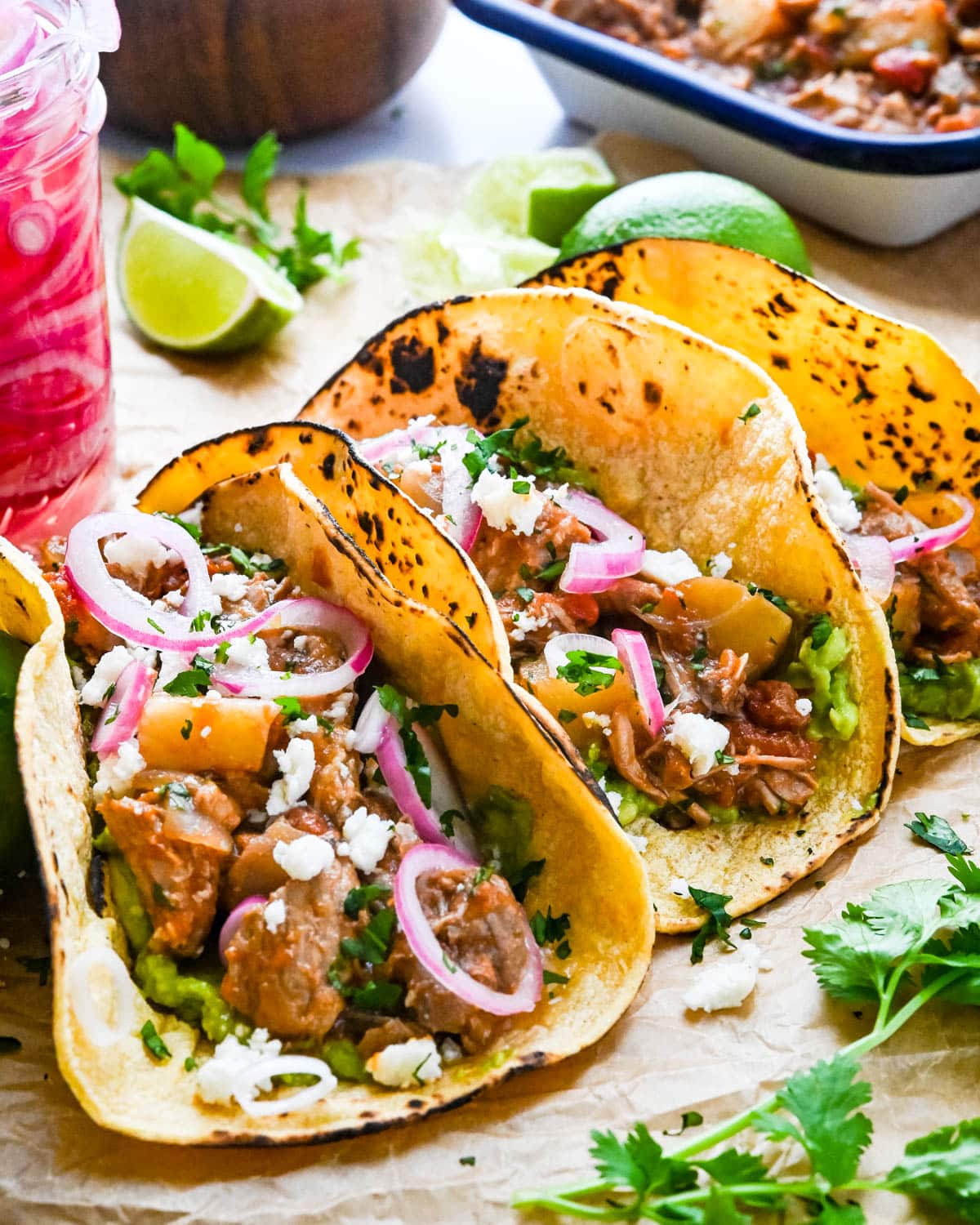 Tinga-style pork tacos with pickled red onions, and limes in the background.