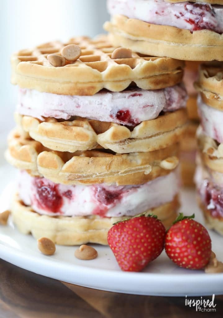 Stack of peanut butter and jelly waffle ice cream sandwiches with berries and peanut butter chips in the background.