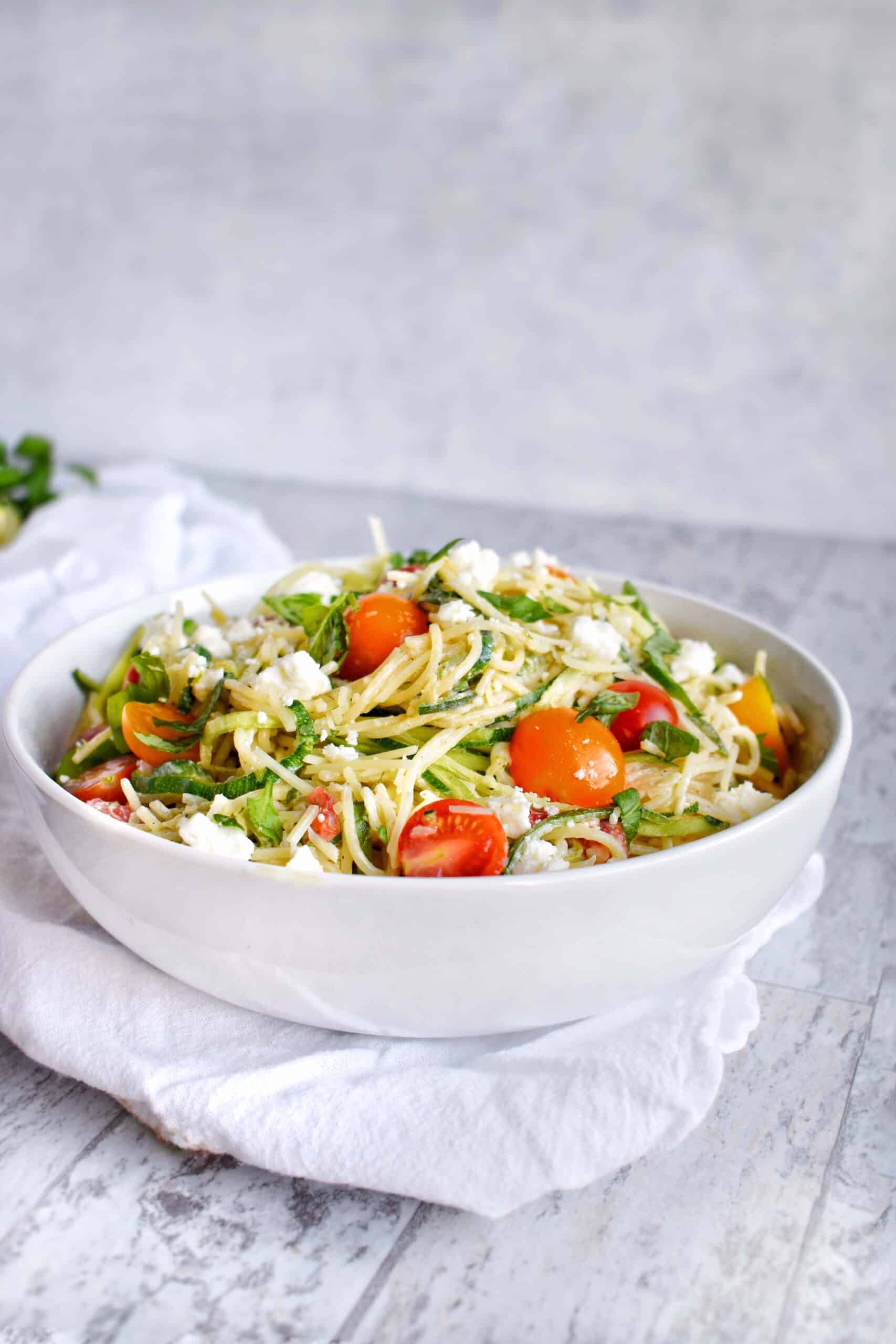 Zucchini noodle pasta with yogurt herb sauce with tomato in a white bowl.