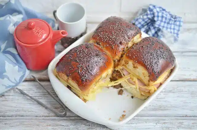 Poppy seed ham and cheese sliders in a white baking dish.