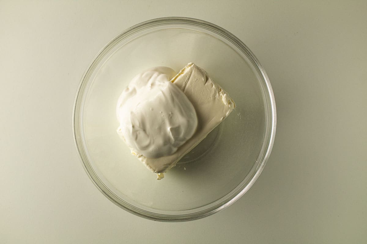 Cream cheese and sour cream in a clear bowl.