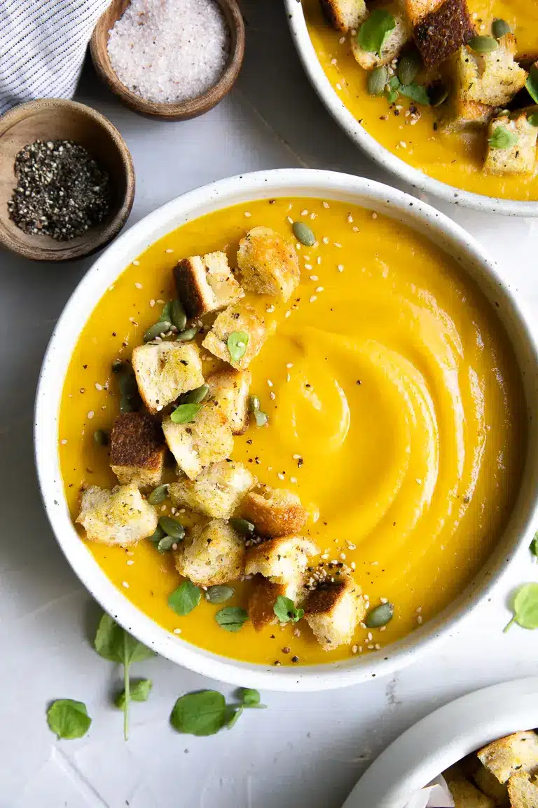 Orange butternut squash soup in a white bowl with croutons on top.