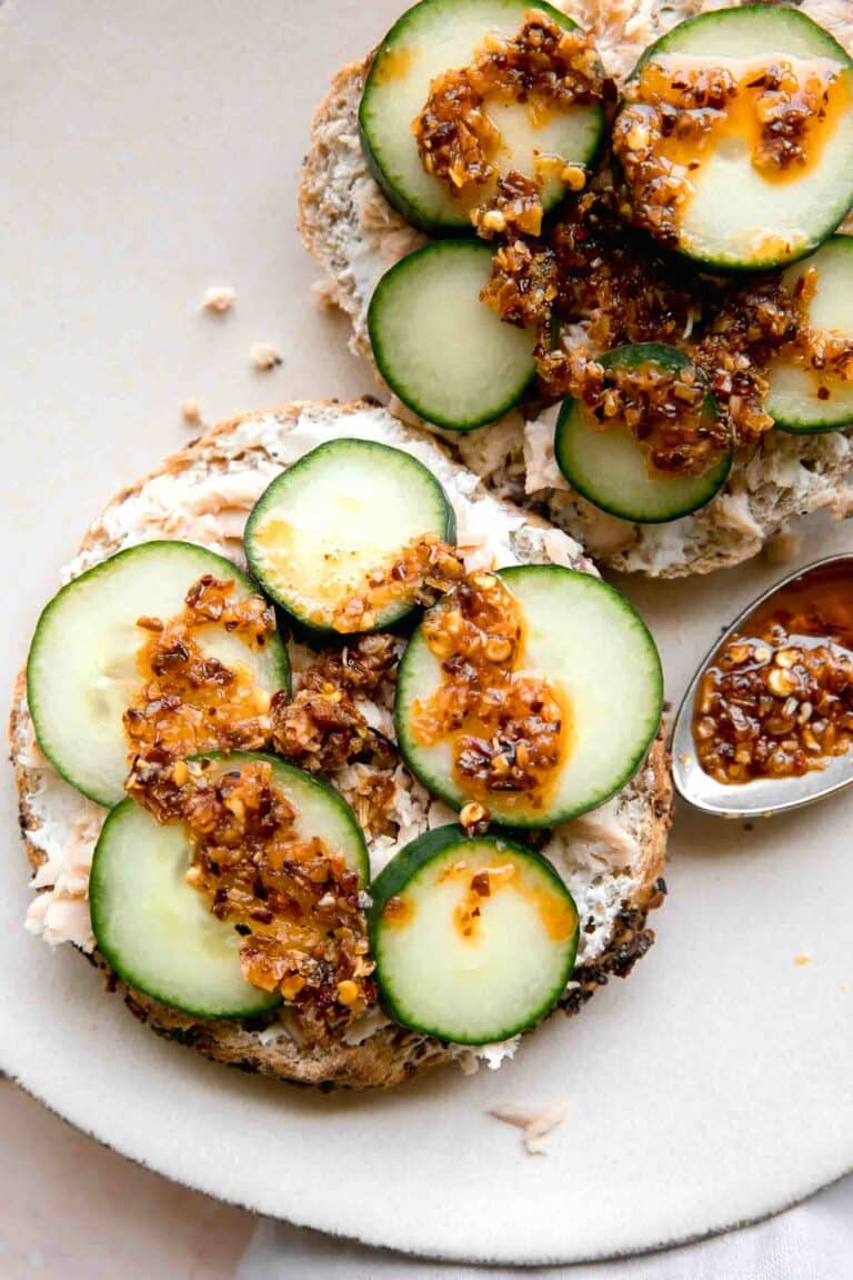 Chili crunch salmon cream cheese bagel with cucumbers on a platter.