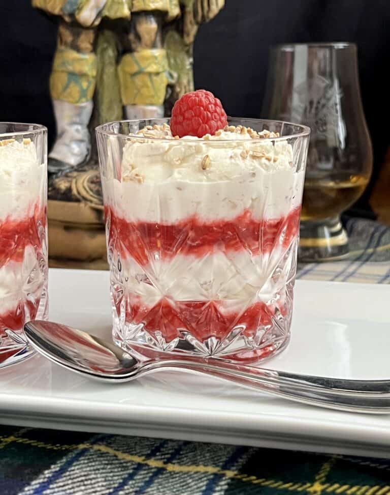 Layered cranachan Scottish dessert in a clear glass on a square plate.