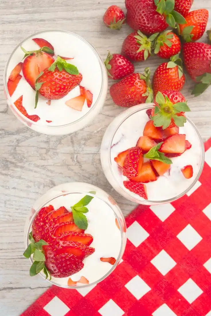 Mexican strawberries and cream in a glass on a wooden surface.