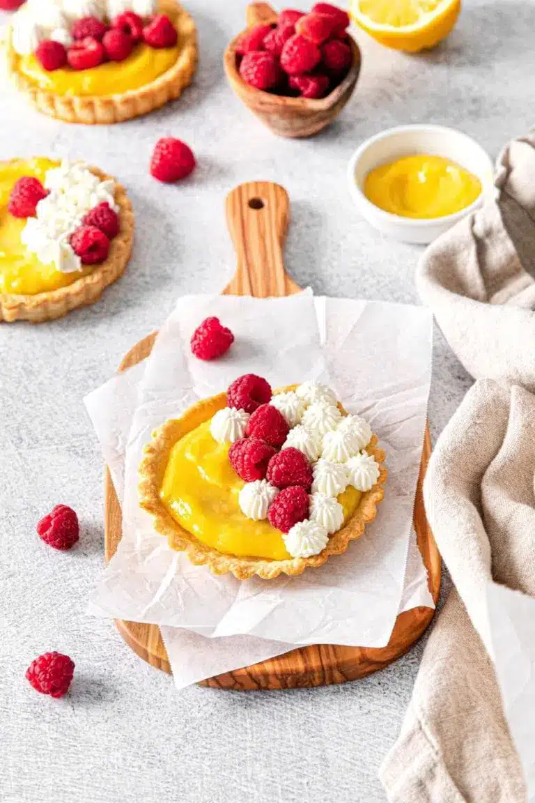 Mini lemon tarts with raspberries on parchment paper.