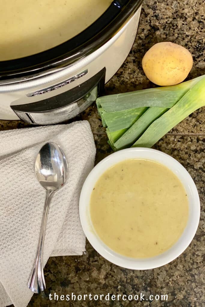 Potato and leek soup in a white bowl ingredients and slow cooker in the background.