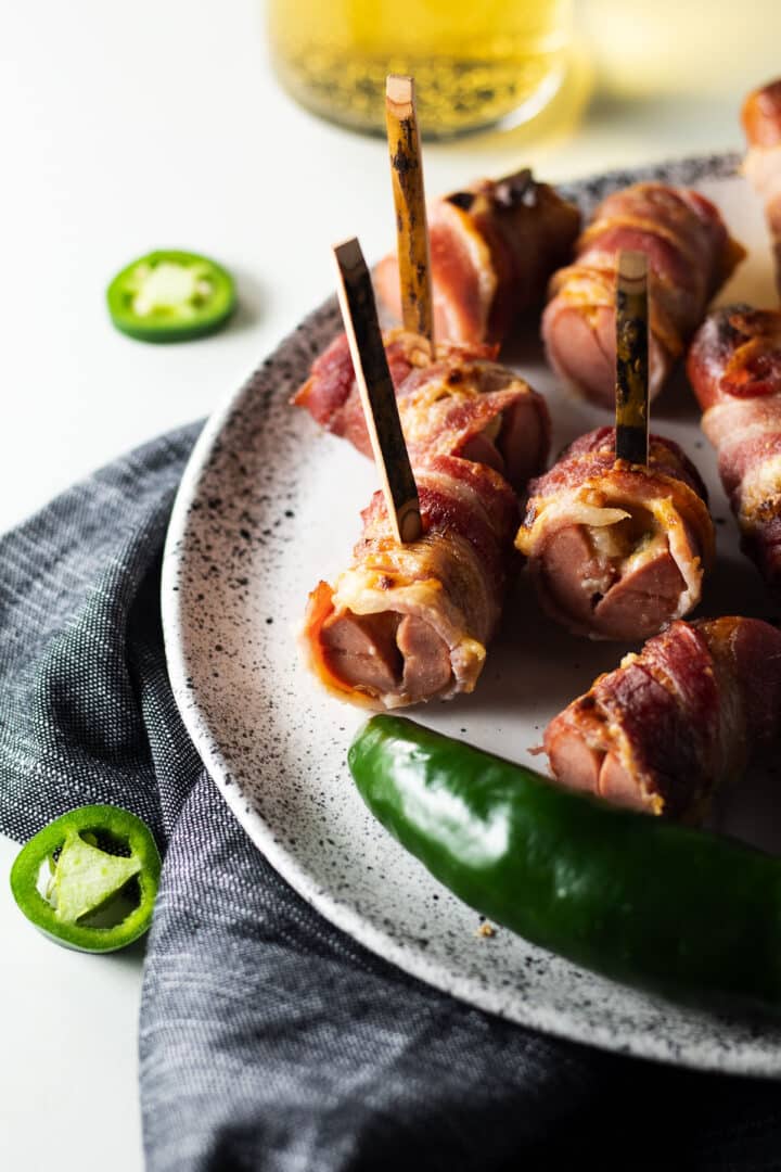 Bite-sized bacon-wrapped jalapeno popper hot dogs on a white speckled plate.