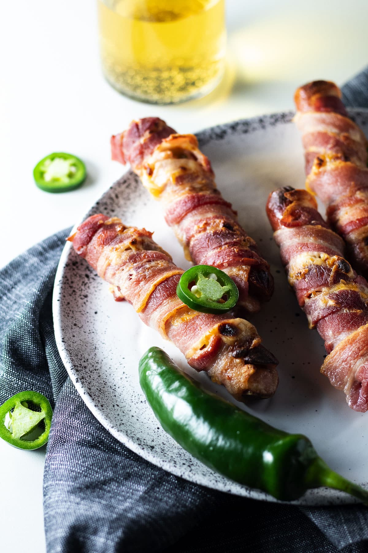 Bacon wrapped jalapeno popper hot dogs on a white speckled plate.