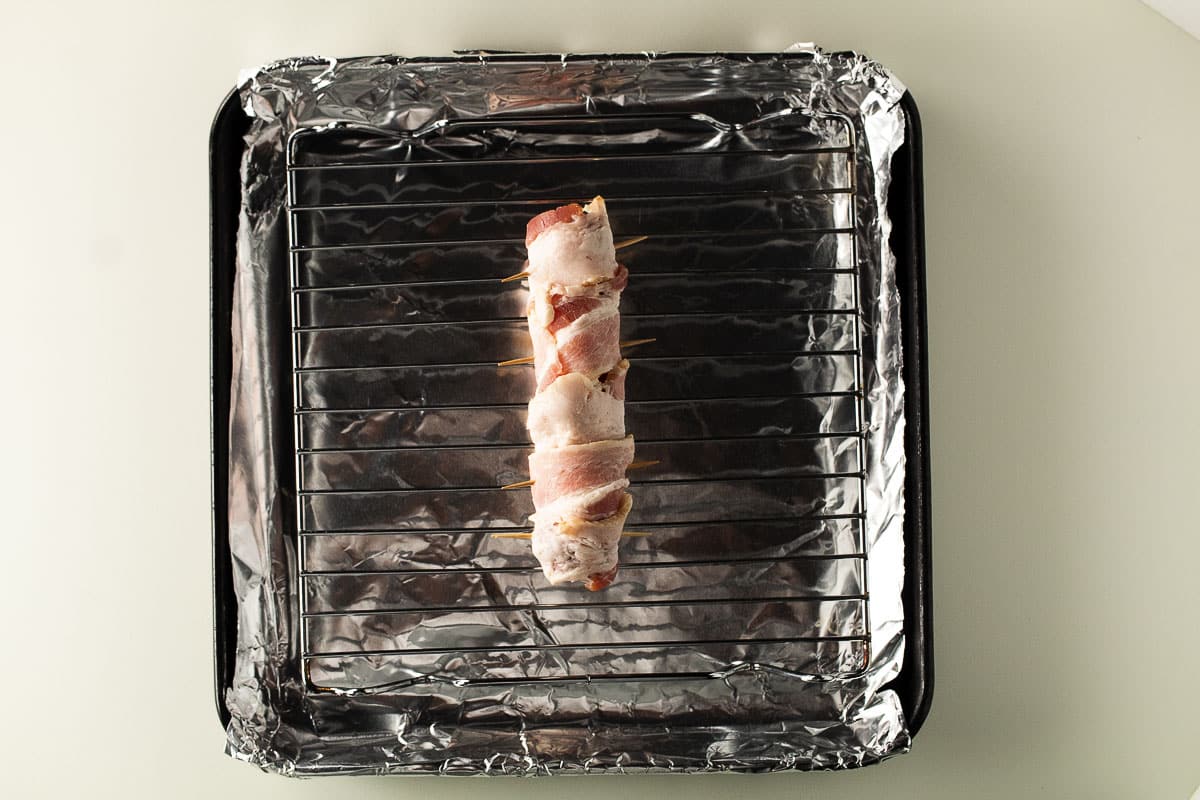 Bacon wrapped hot dog on baking rack.