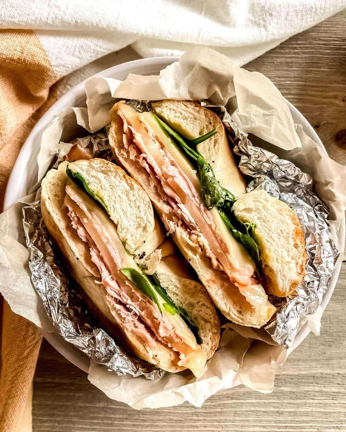 Baked ham and cheese bagel sandwich in aluminum foil.