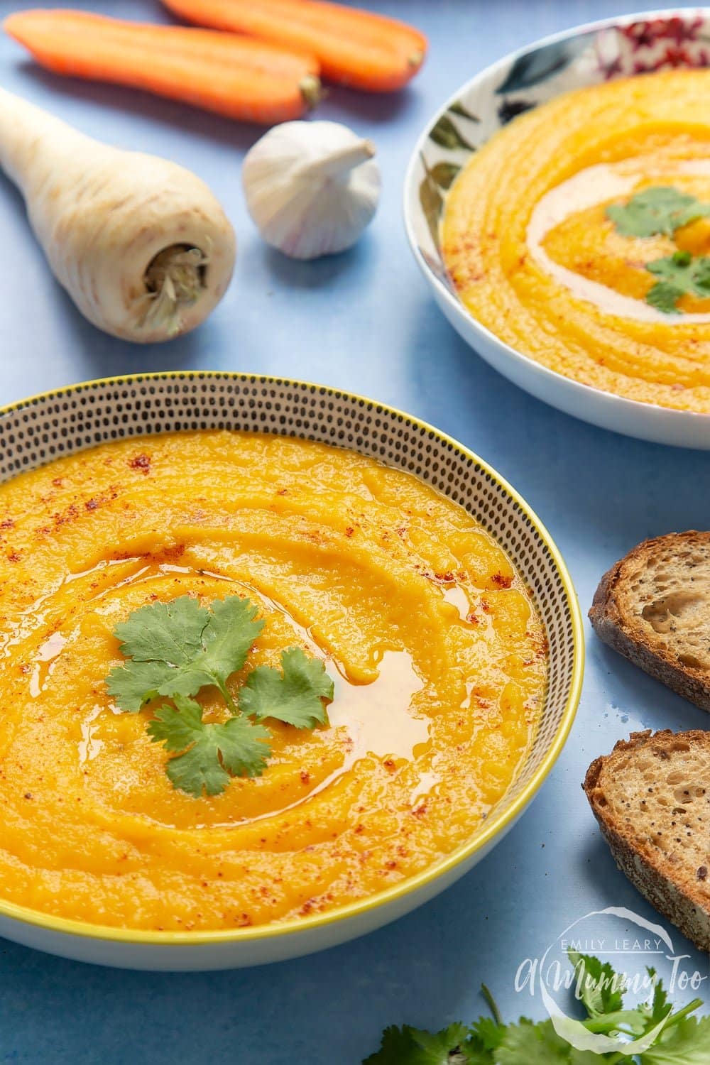 Parsnip and carrot soup in a bowl with ingredients surrounding it.