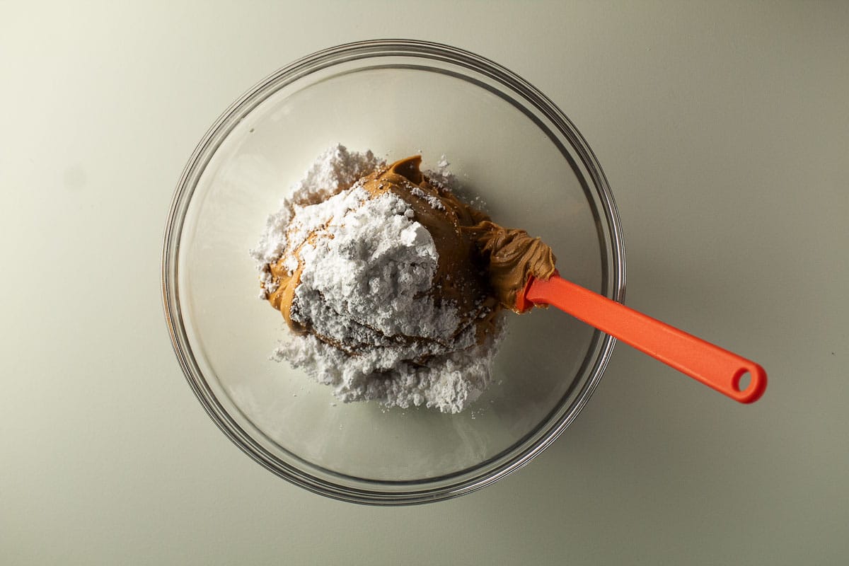 Peanut butter and powdered sugar in a clear mixing bowl.