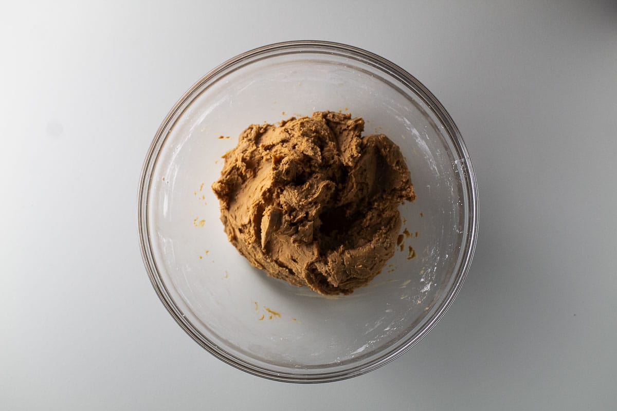 Peanut butter cookie dough in a clear bowl on a white background.