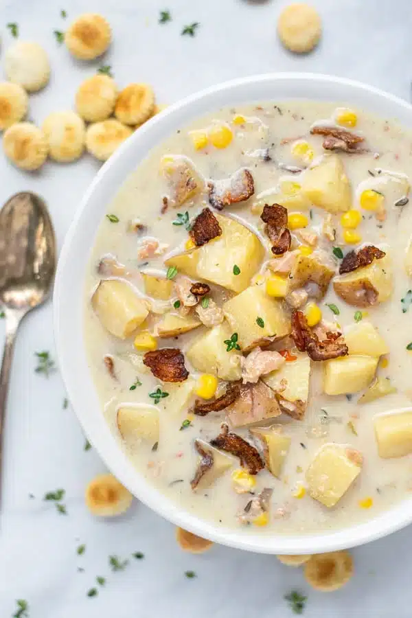 New England slow cooker clam chowder in a white bowl with crackers and bowls.