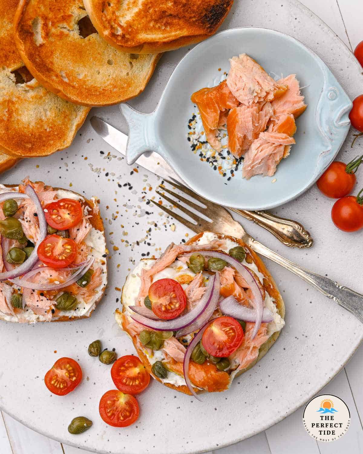 Smoked salmon and egg breakfast bagel toast on a white speckled platter.