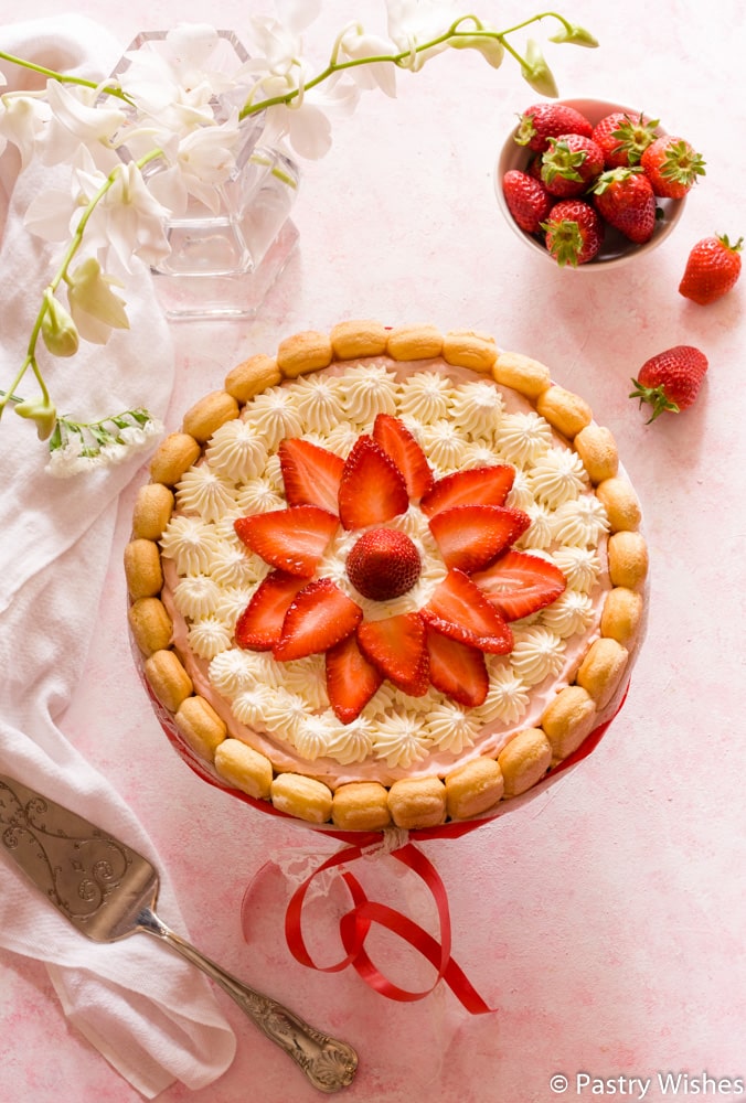 Strawberry Charlotte cake on a tray with strawberry slices and more strawberries in the background.