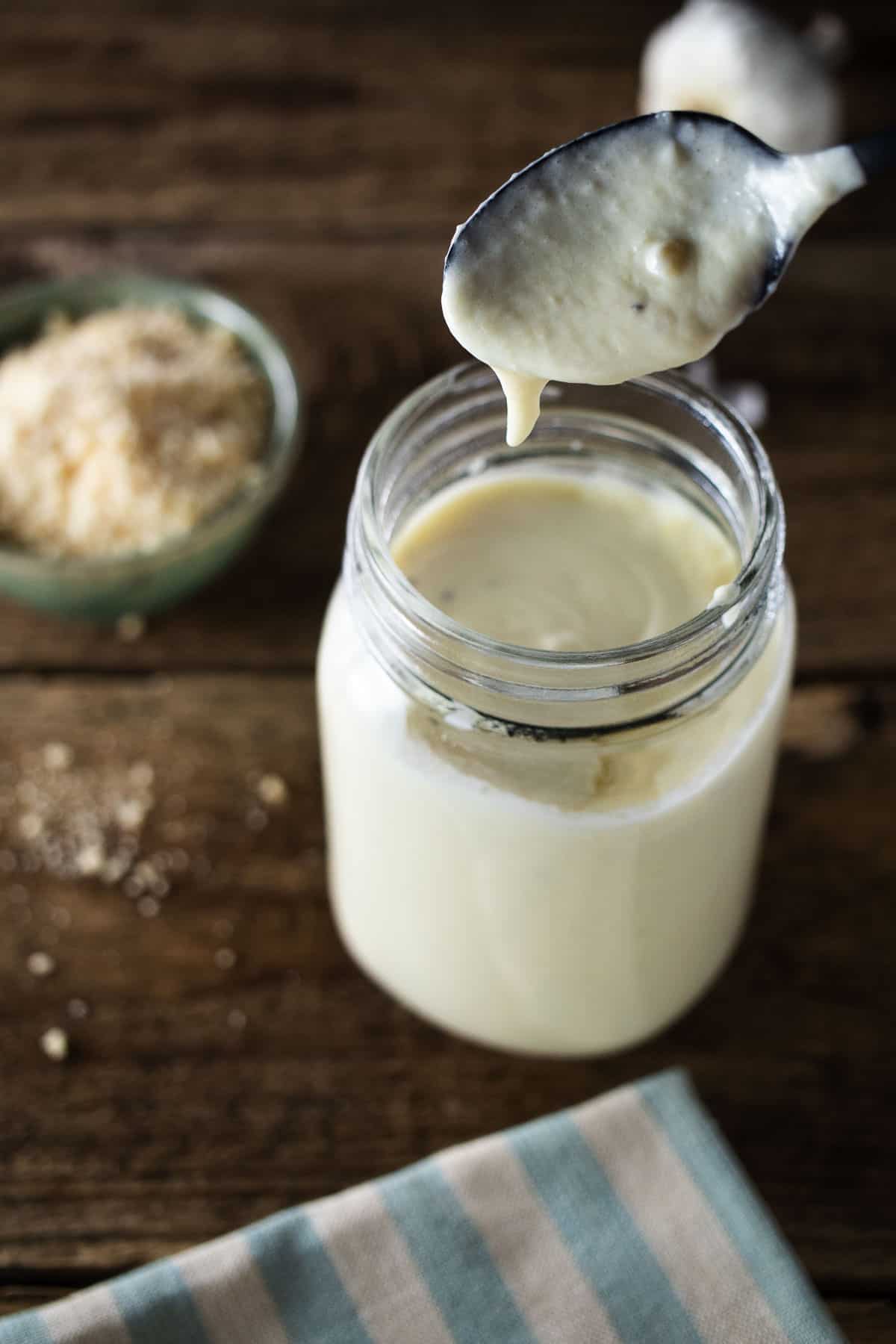 Spoon dipping into jar into alfredo sauce.