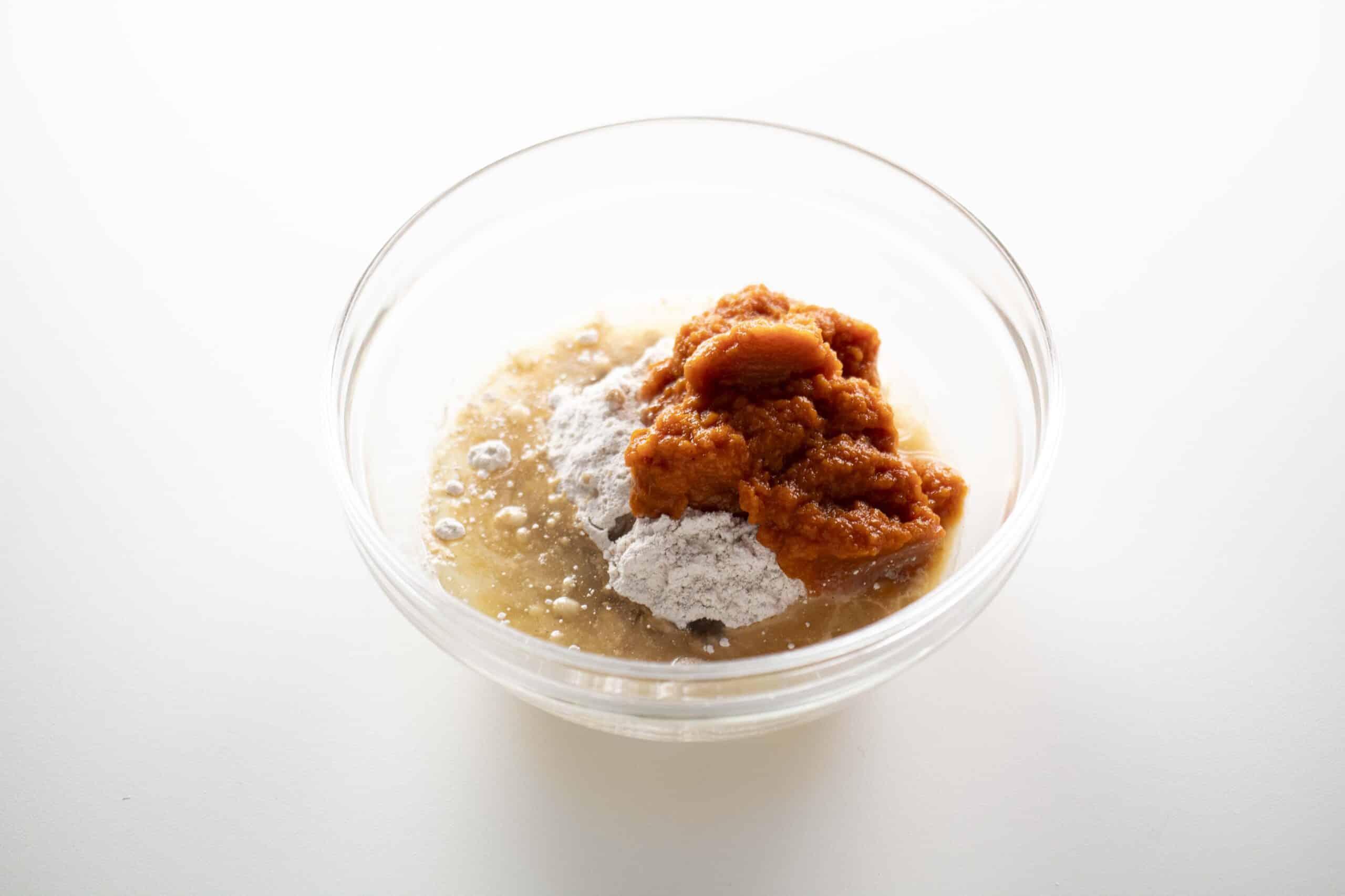 Ingredients for pumpkin spice donuts in a clear bowl.