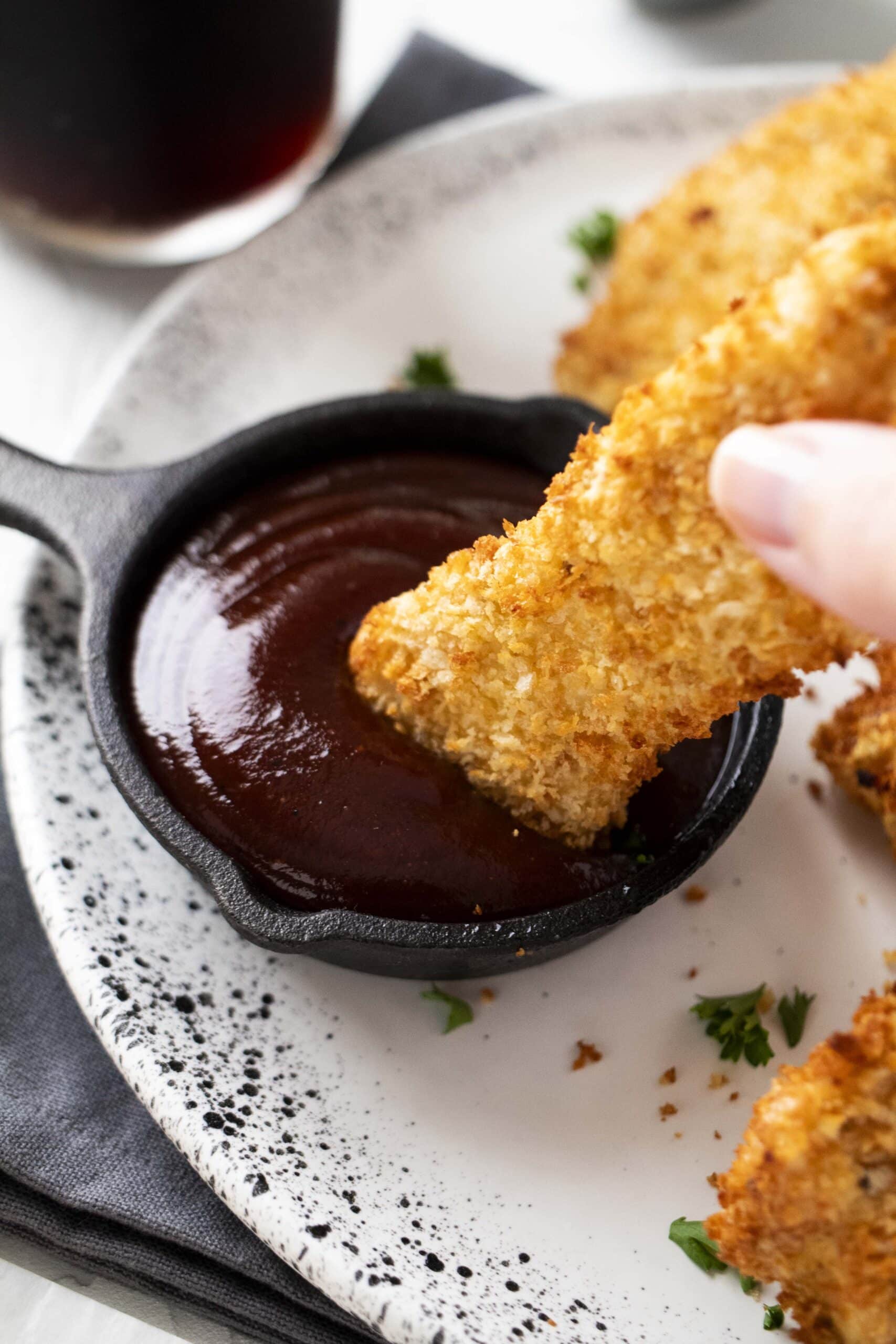 Hand dipping chicken tender in bbq sauce.