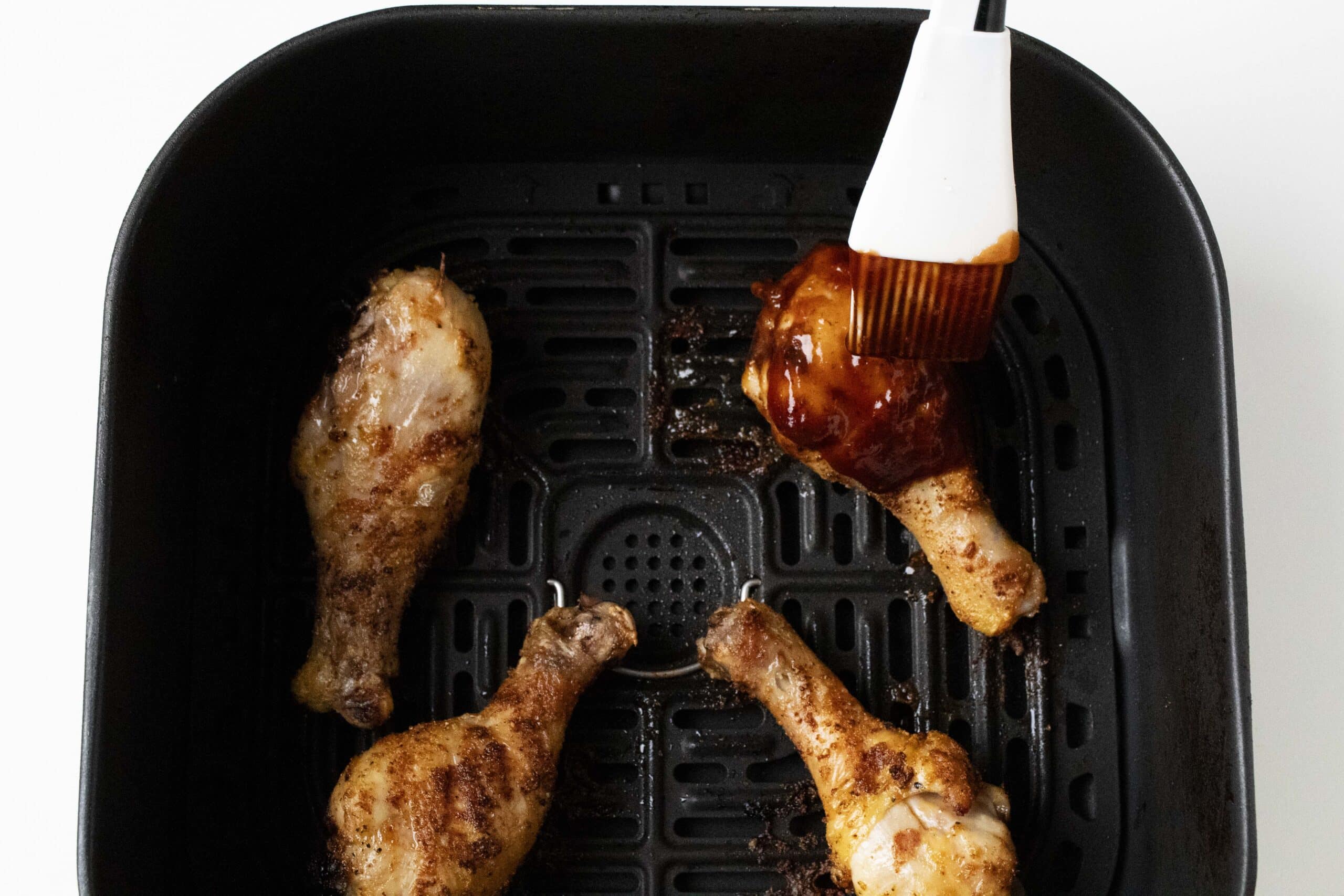 Brushing air fryer chicken legs with barbecue sauce.