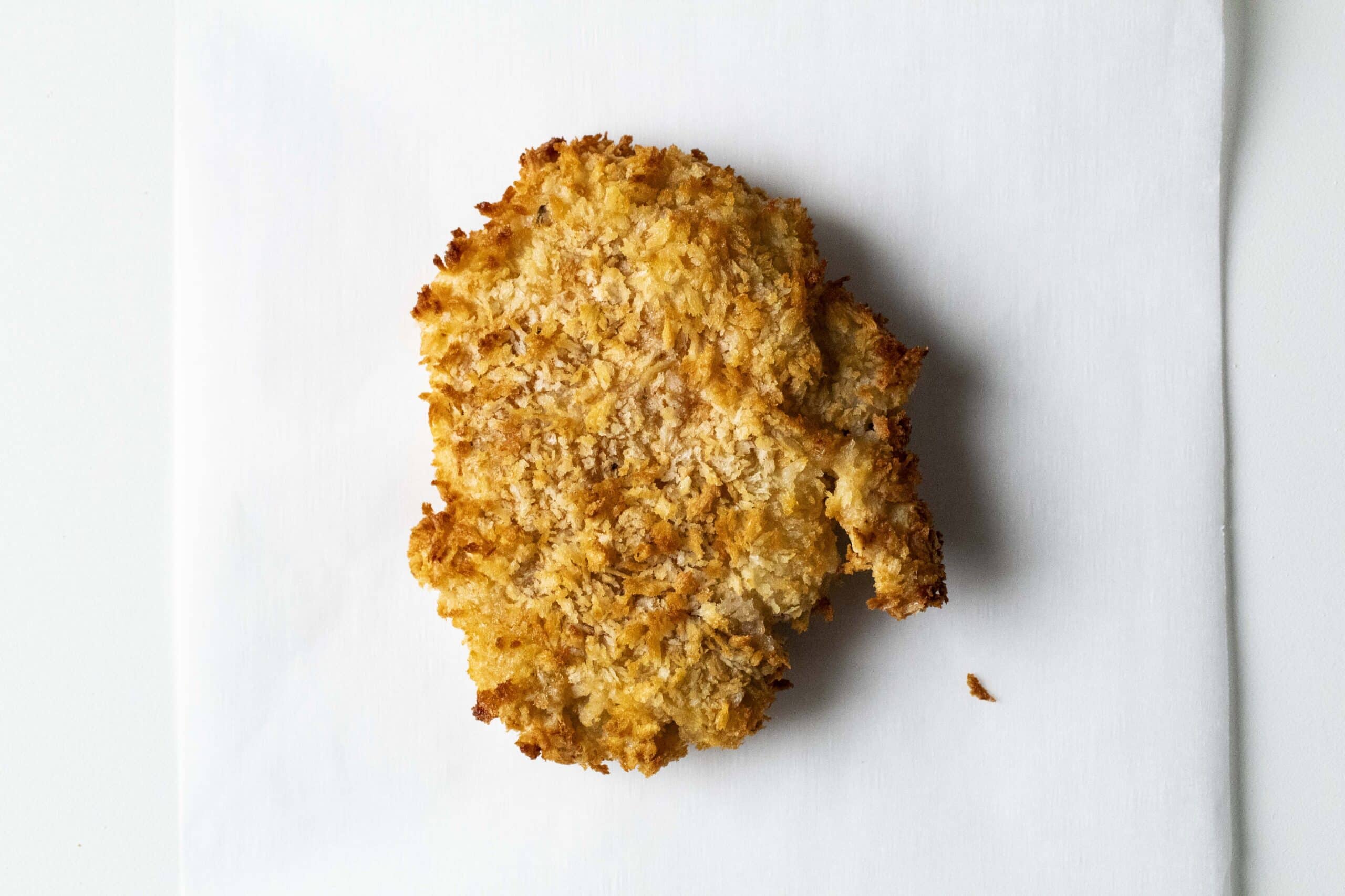 Cooked breaded chicken thigh on a white surface.