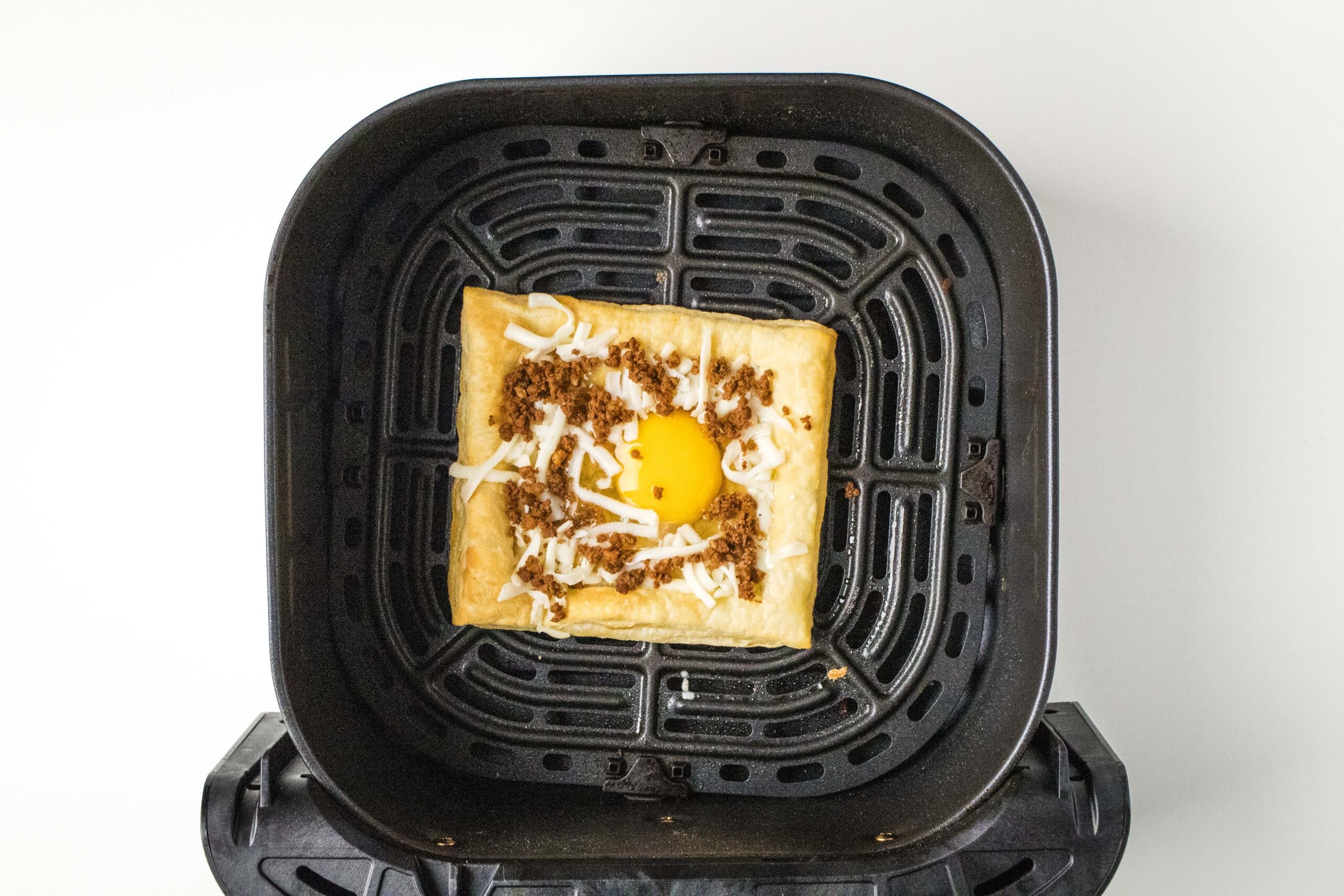 Uncooked puff pastry air fryer Mexican breakfast pizza in the air fryer basket.