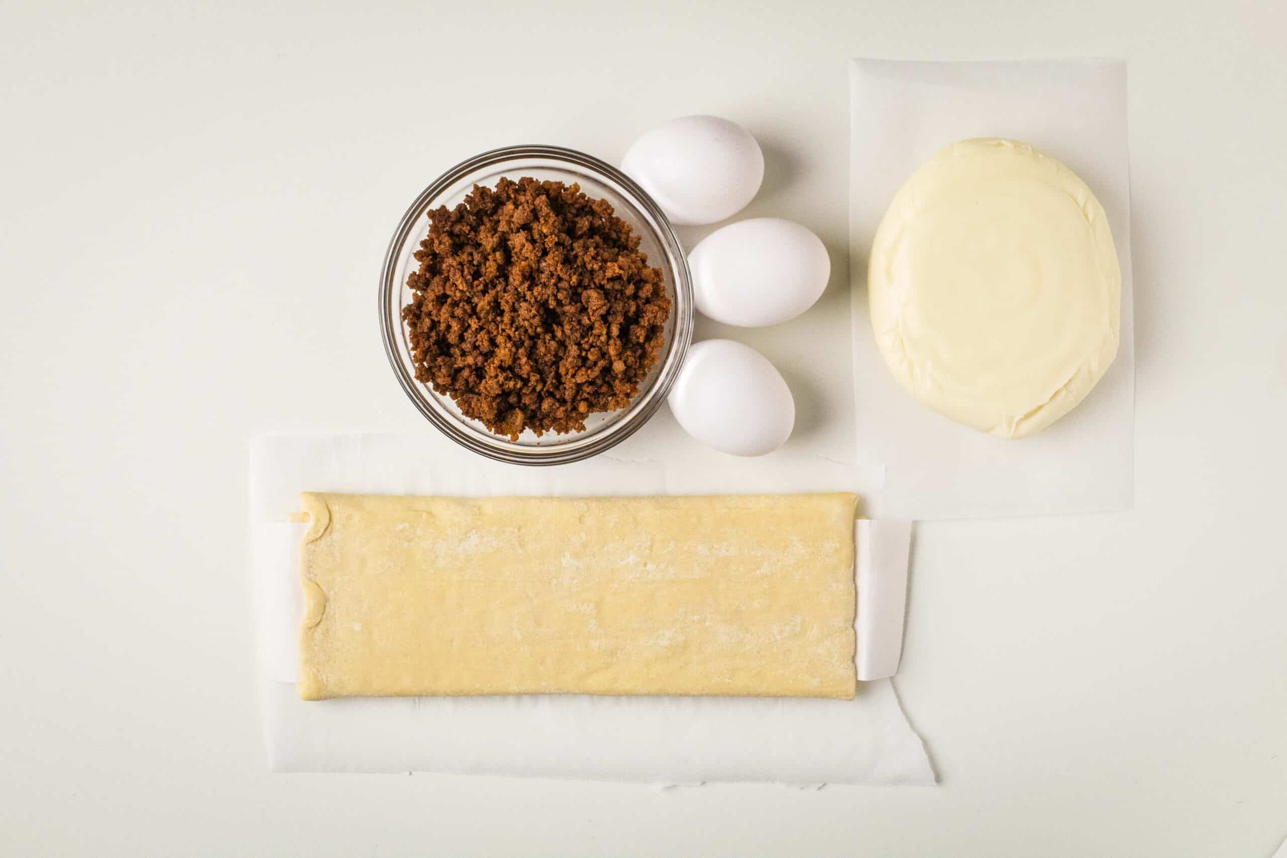 Puff pastry, chorizo, eggs, and Oaxaca cheese on a white background.