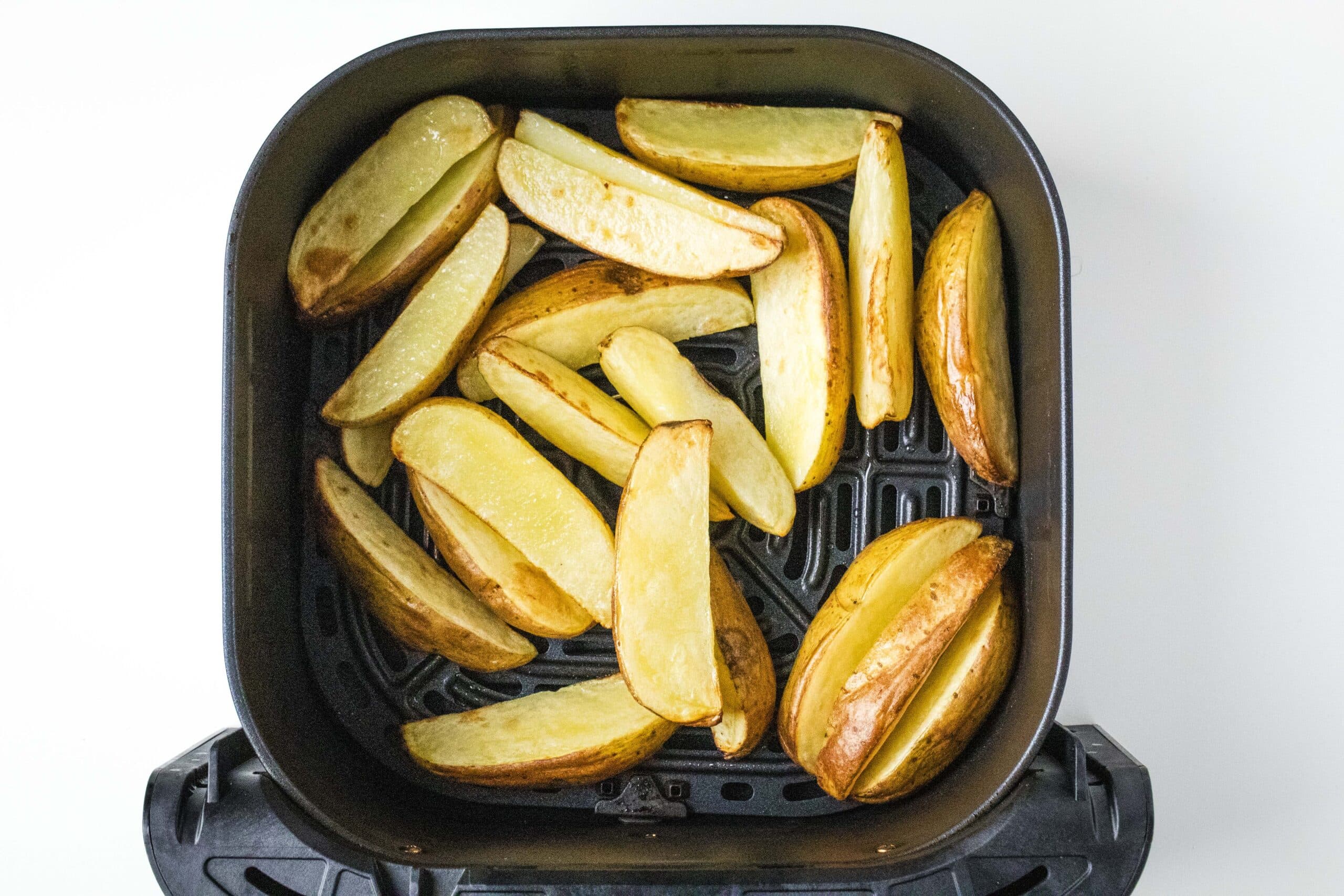 Par cooked potato wedges in air fryer basket.