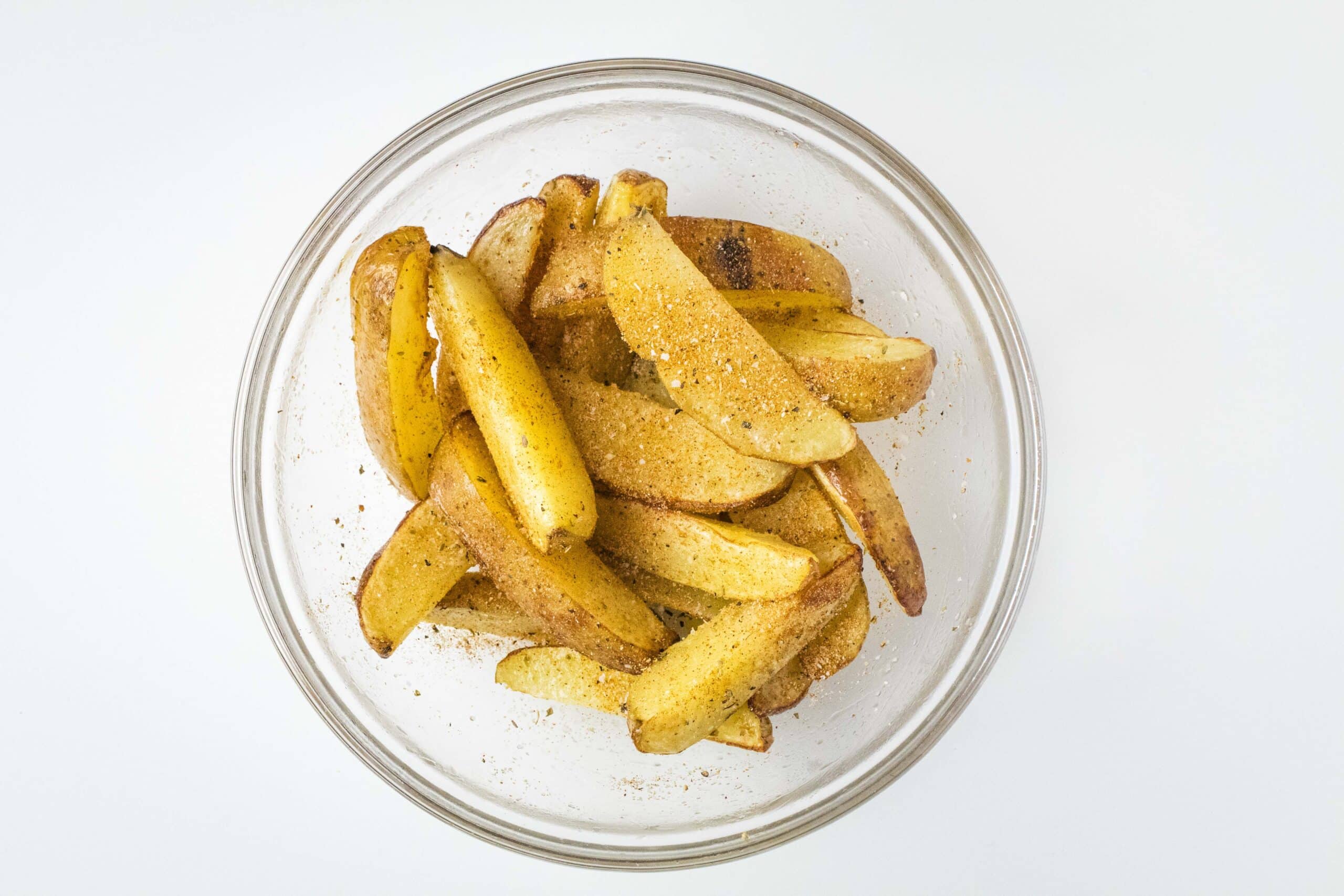 Seasoned par-cooked potato wedges in a glass bowl. 