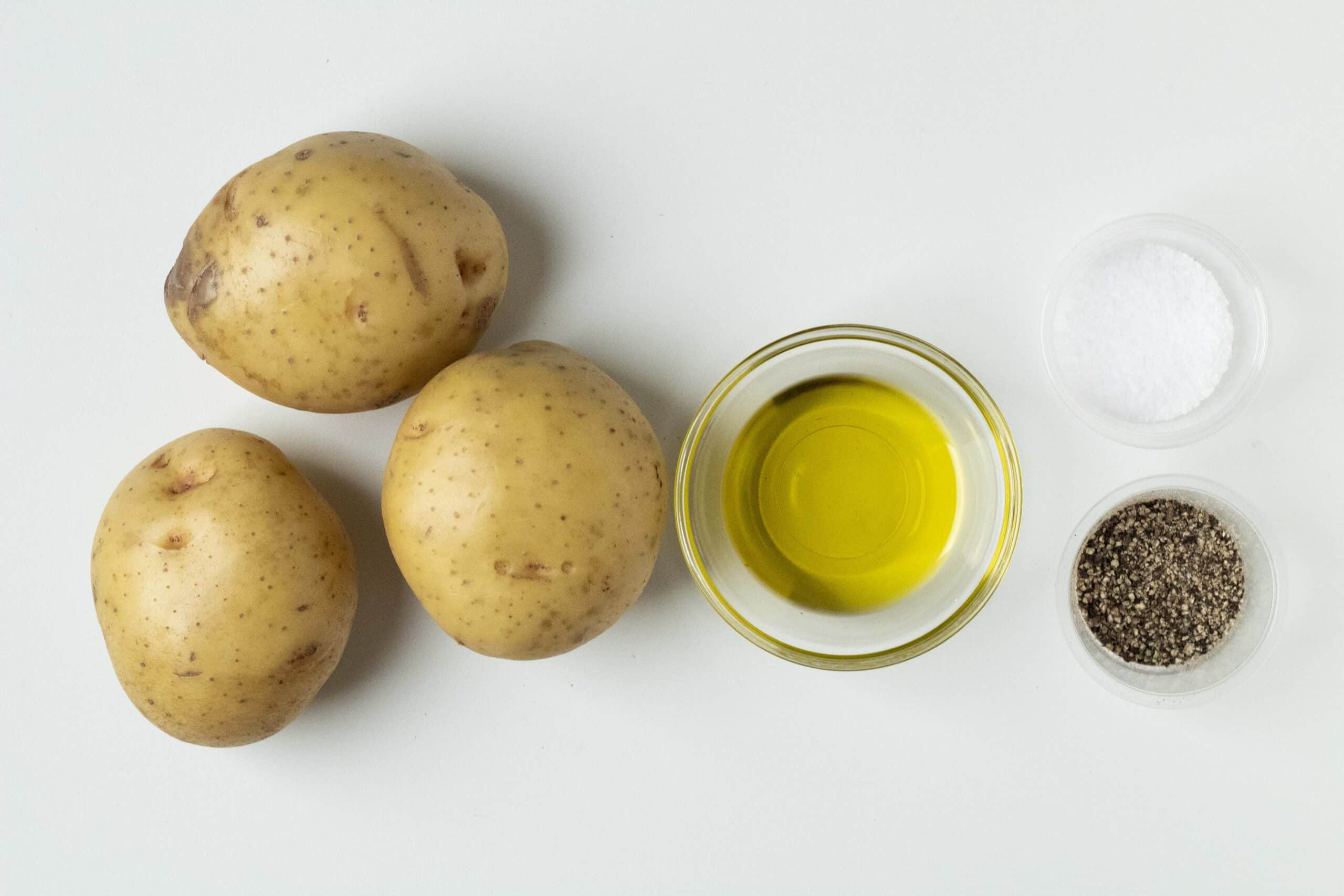 Yellow potatoes, olive oil, salt, and pepper on a white background.